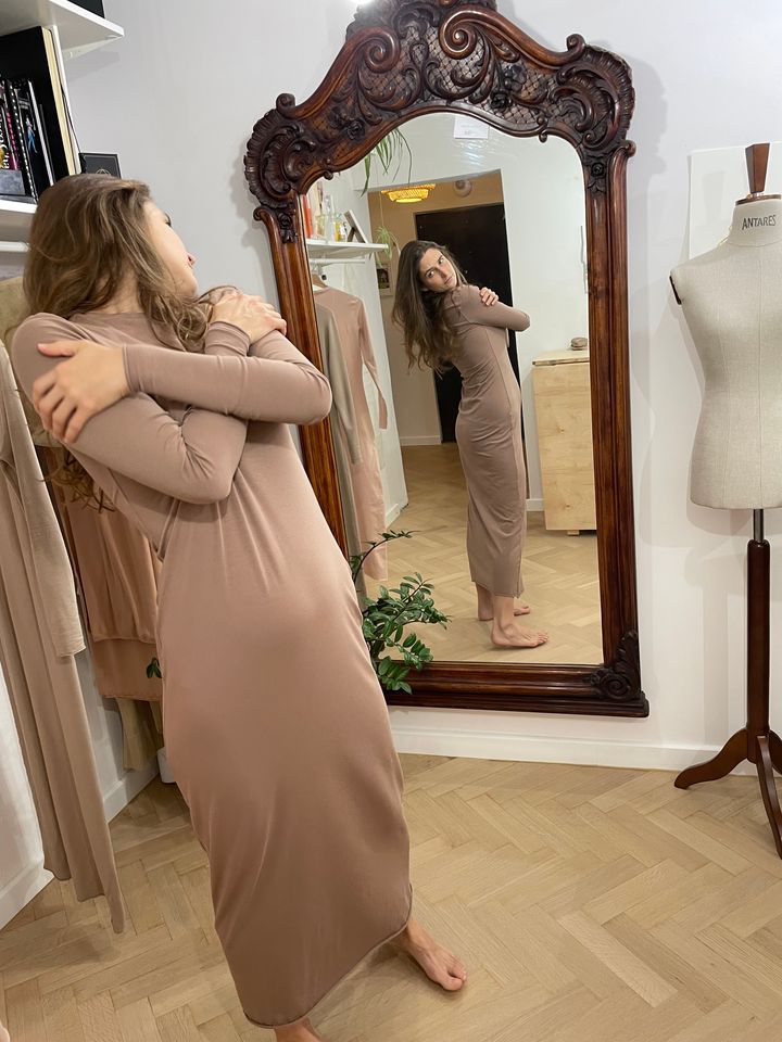 kobieta ubrana w beżową długą sukienkę przegląda się w lustrze